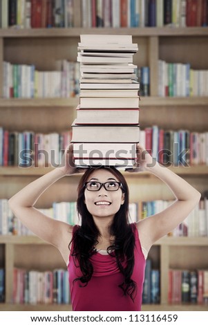 Portrait of female college student carrying a pile of books over her head. shot in library