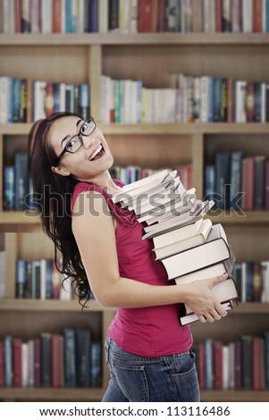 Attractive young female college student carrying a stack of books in the library