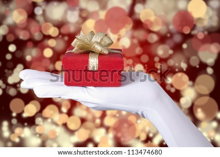 Woman\'s hand with gloves holding a Christmas gift over unfocussed light background