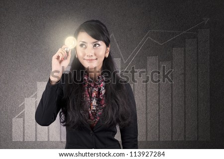 Beautiful asian businesswoman with glasses holds a light bulb over diagram background