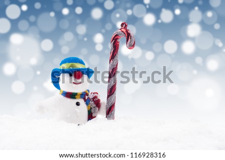 Snowman doll with candy cane on the snow with blue christmas light background