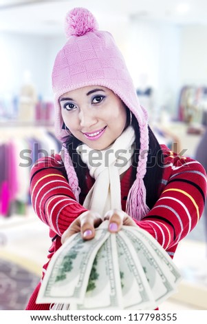 Young woman giving US dollar bills cheerfully wearing winter outfit