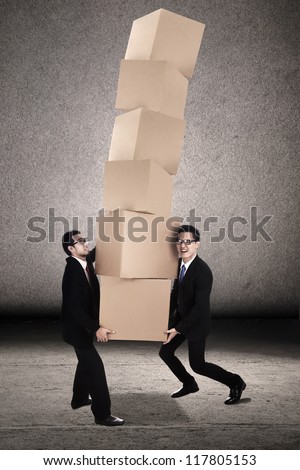 Teamwork photo concept: Two businessmen trying to balance plenty of boxes together