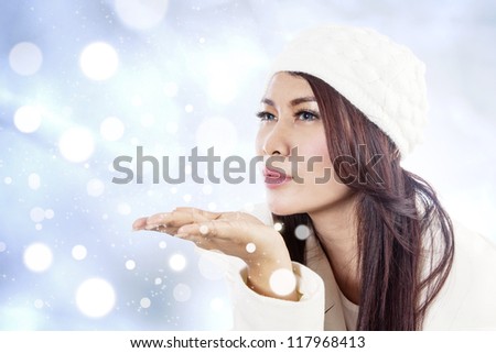 Beautiful young lady blowing snowflakes on blue unfocused lights background