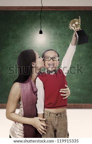 A mother is kissing her son for winning a trophy at school