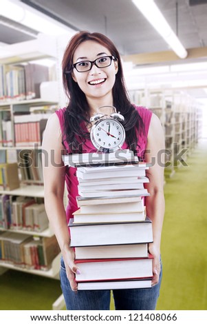 Young female student carrying stack of books with a clock on top