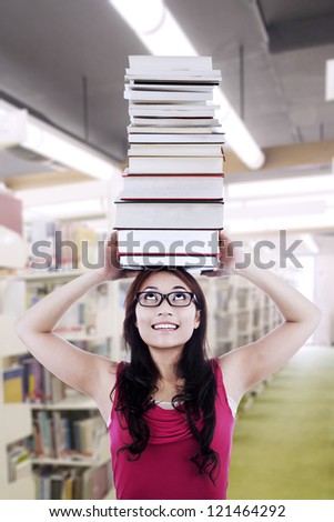A beautiful nerd girl student wearing glasses is holding stack of books on top of her head