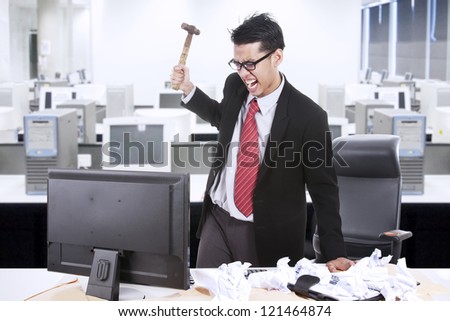 Angry businessman is about to throw a hammer at his computer in the office