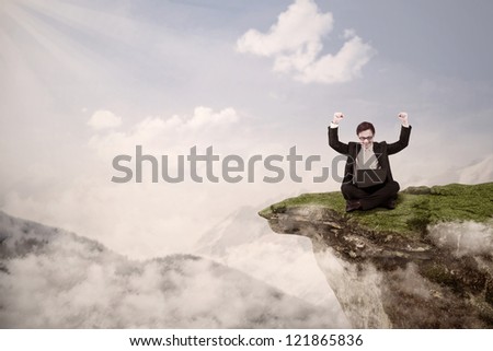 Picture of businessman with arms raised while sitting with his laptop on a mountain high