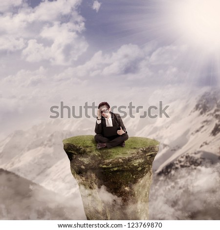 Picture of thinking businessman sitting with his laptop on a mountain rock