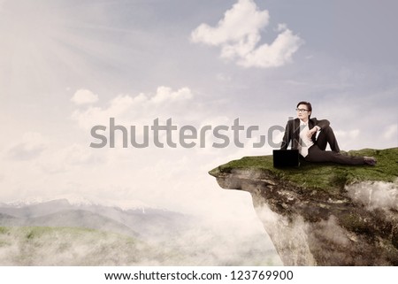 Young businessman is sitting with his laptop on top of a mountain