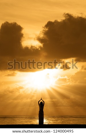 Silhouette of young woman is doing yoga at sunrise