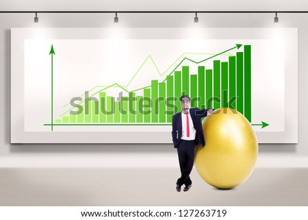 Businessman is standing beside a big golden egg on profit bar chart background