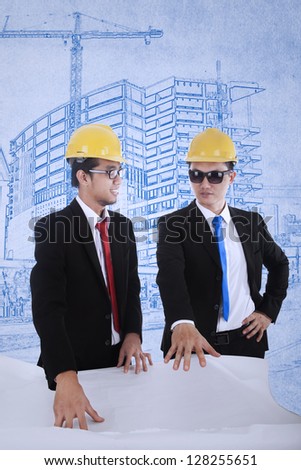 Young architect and supervisor are reviewing plans over blueprints background