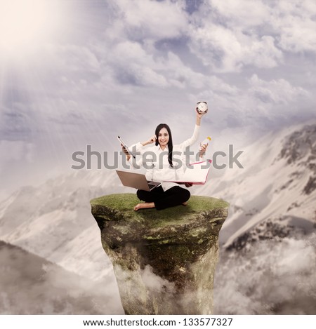 Young entrepreneur is multitasking on top of a mountain rock