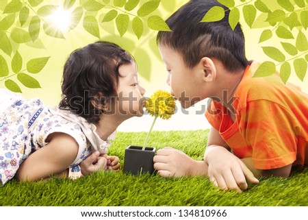 Brother and sister kissing a yellow flower in the park