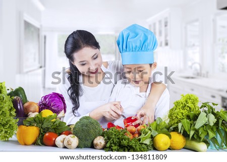 Young mother teach her son to cut vegetables at home