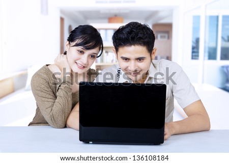 Happy couple looking at laptop, surfing the internet in living room