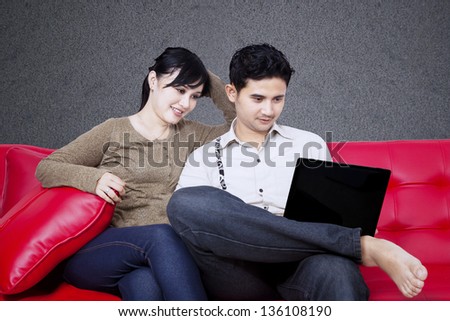 Happy couple looking at laptop on sofa with black background
