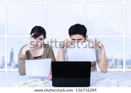 Asian couple sad looking at laptop in office