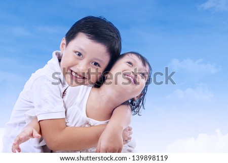 Cute brother and sister hugging under blue sky