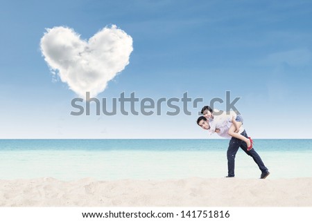 Boyfriend giving piggyback ride under heart cloud on the beach