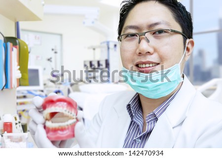 Asian dentist is showing braces on fake teeth at the clinic