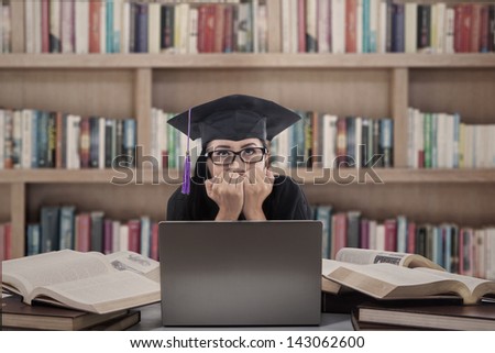 Asian female graduate biting her nails in front of laptop at the library