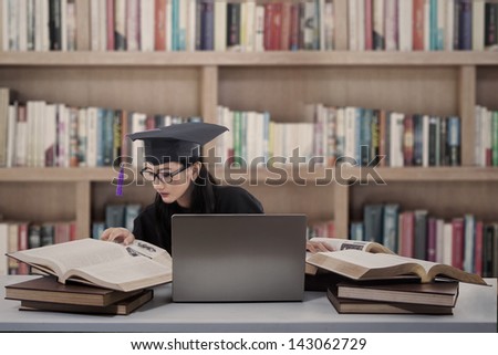 Busy female graduate is reading books at library