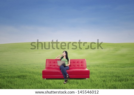 Pensive woman sitting on red sofa at green meadow