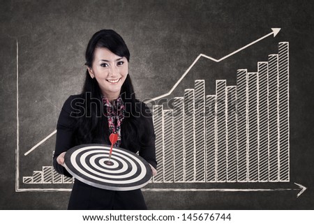 Businesswoman hold bull\'s eye on growing bar chart chalkboard as the background