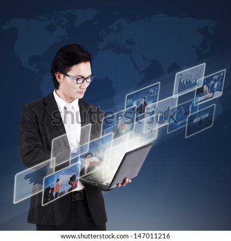 Asian businessman working on his laptop and searching online pictures on blue world map background