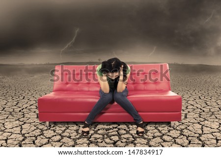 Picture of stress female  on red sofa with dry soil under bad weather