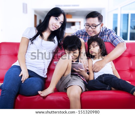 Happy family is enjoying weekend break on red sofa at home