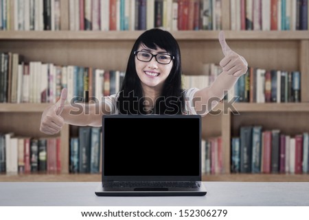 Portrait of happy college student giving thumbs up with copy space on laptop. shot in library