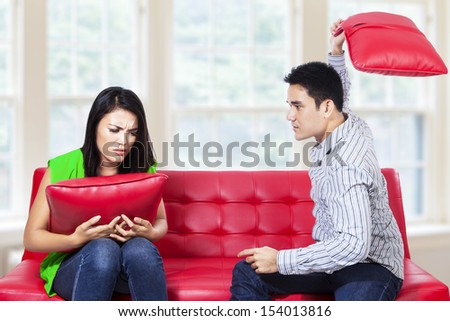 Angry couple on red sofa fighting with pillow in the living room