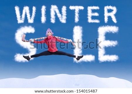 Woman jumping in winter sale sign on blue sky