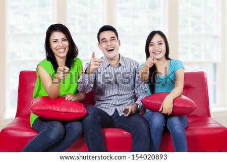 Three friends pointing at the camera and smiling at home