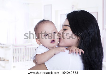 Young asian mother kissing her adorable baby at home