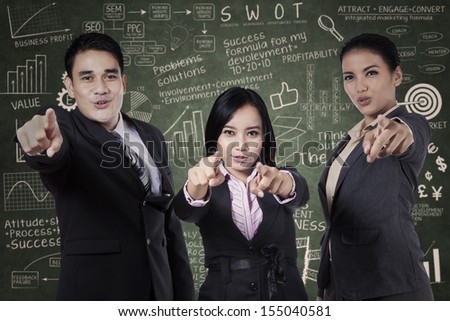 Excited young business people pointing at you on chalkboard