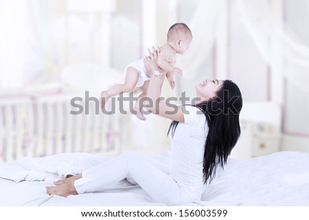 Asian Woman In Bedroom Lifting A Baby Into The Air