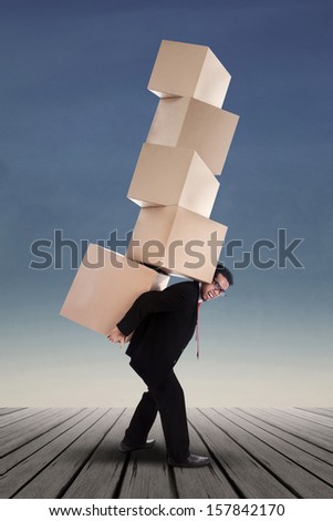 Businessman lifting boxes vertical on the blue sky background