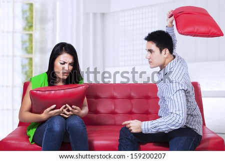 Angry couple on red sofa fighting with pillow in the living room