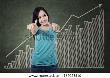 Smiling asian woman giving thumbs up with growth graph