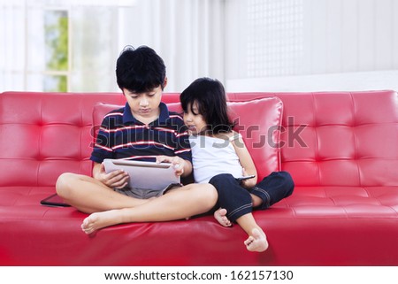 Asian brother and sister using a tablet computer on the couch