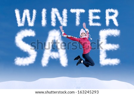 Happy woman jumping with a winter sale sign on blue sky