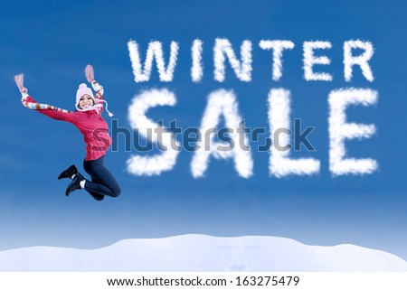 Happy asian girl jumping make the winter sale word on the blue sky