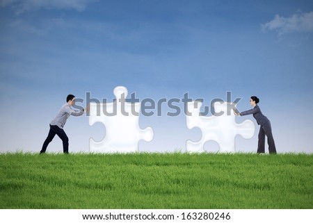 Two business people putting together two puzzle pieces on the meadow