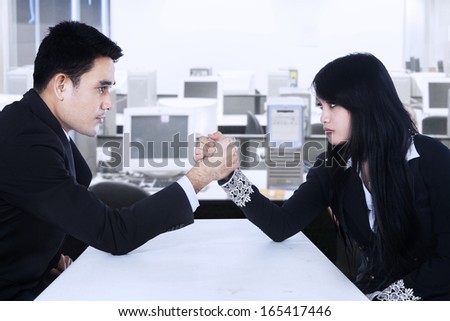 Man and woman in arm wrestling gesture on working table during meeting