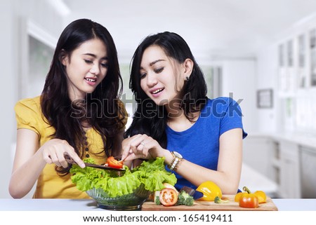 Young asian women prepare salad together in the kitchen